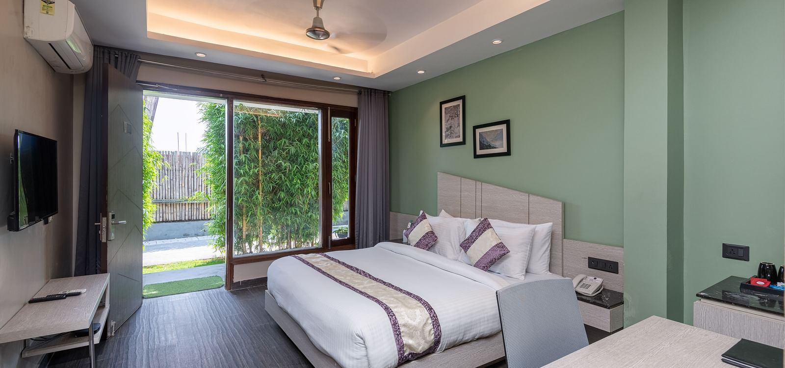 Spacious room at DLS Forest Vines Resort featuring a large bed, a bedside table, a table with chairs, and a large glass door leading to the balcony.