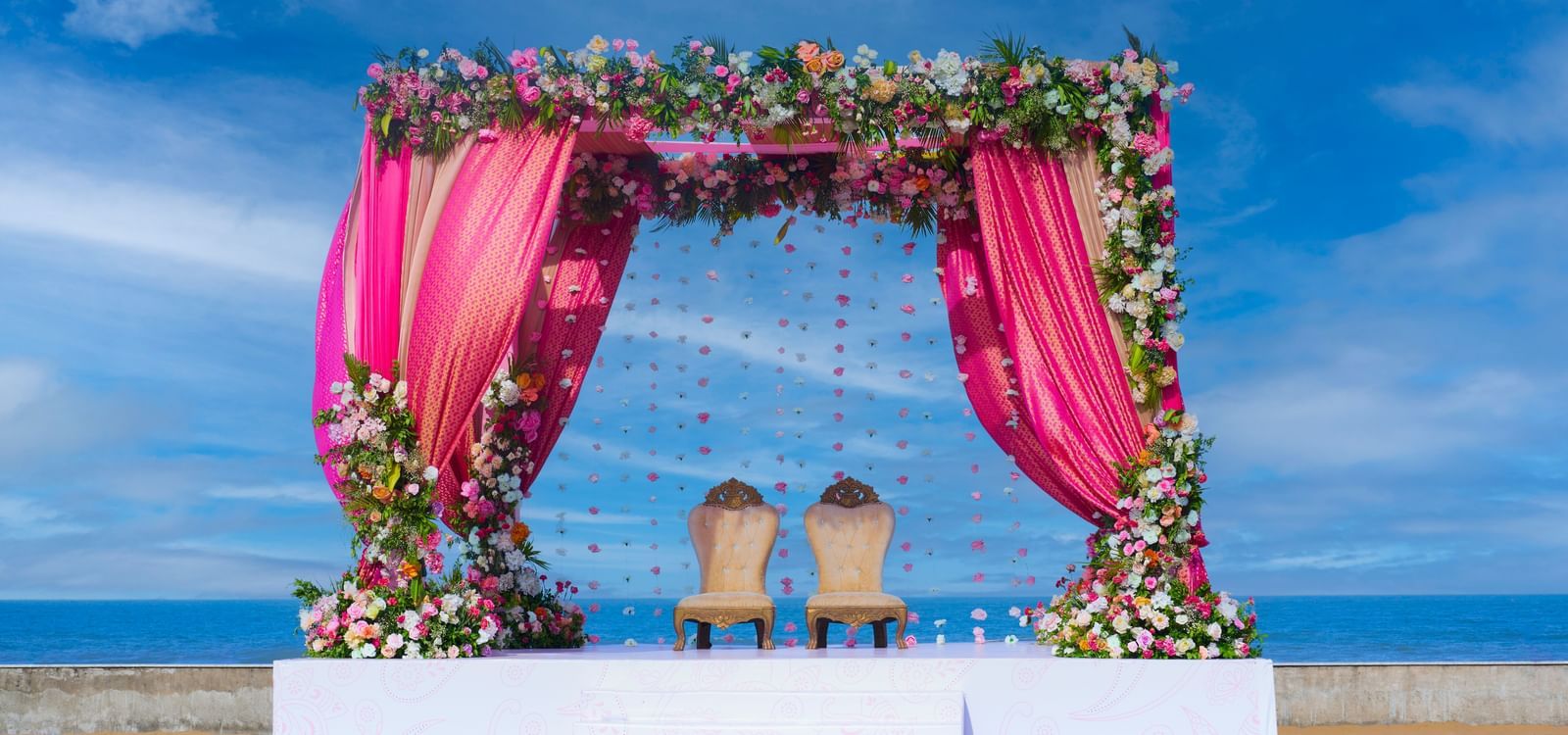 An outdoor platform stage with two chairs under the decorated patio with flowers  featuring the blue sky & sea at the backdrop at Grande Bay Resort & Spa.