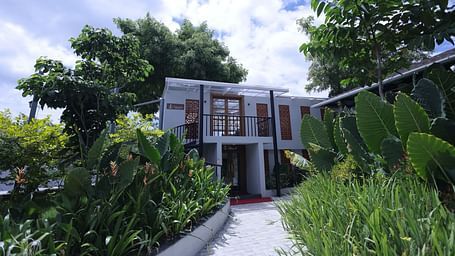 Exterior view of a villa surrounded by lush plants and trees at Trishvam Symphony, Krishnagiri.