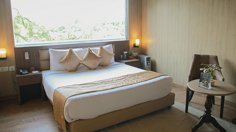 A plush bed with a wide window above the headboard and a chair and a coffee table next to it