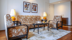 A cosy seating area with a sofa, two chairs, a glass coffee table, and lamps, complemented by framed artwork on the walls - Balaji Sarovar Premiere, Solapur