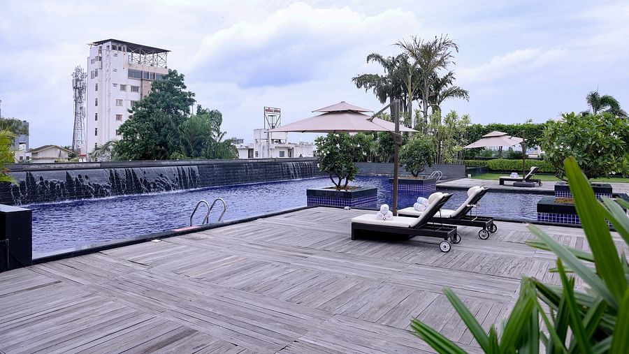 A serene poolside area with lounge chairs, umbrellas, and a calming water feature with lush greenery in the background - Balaji Sarovar Premiere, Solapur