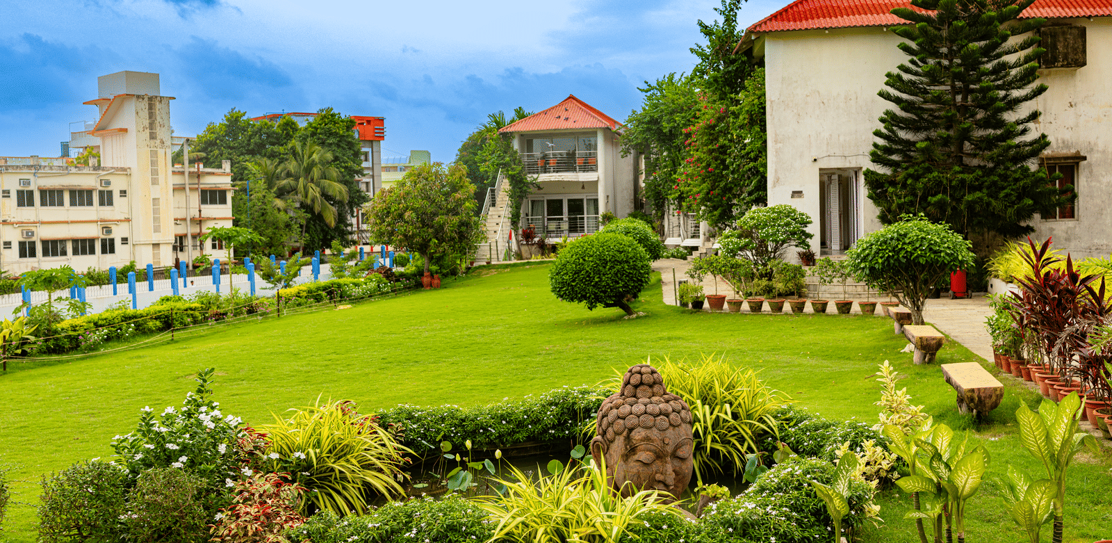 Large white resort buildings with a spacious, manicured green lawn, garden area, and trees - Hotel Seagull Digha