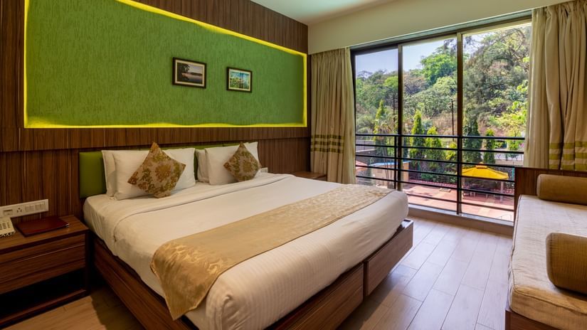 Picture showing the King size bed in the Premium Deluxe Suite with a luscious greenery view at ZARA’s Resort, Khandala