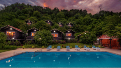 An open-air swimming pool with guest accommodations and a hill with lush green trees in the background - Highland Sarovar Portico, Sindhudurg