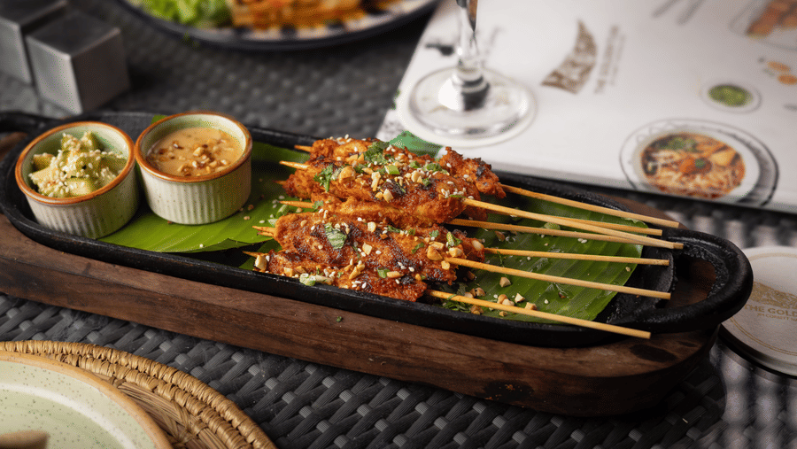  A platter of food including skewers of grilled meat, small side dishes, and a glass of wine, on a set table  at The Golden Tusk, Jim Corbett