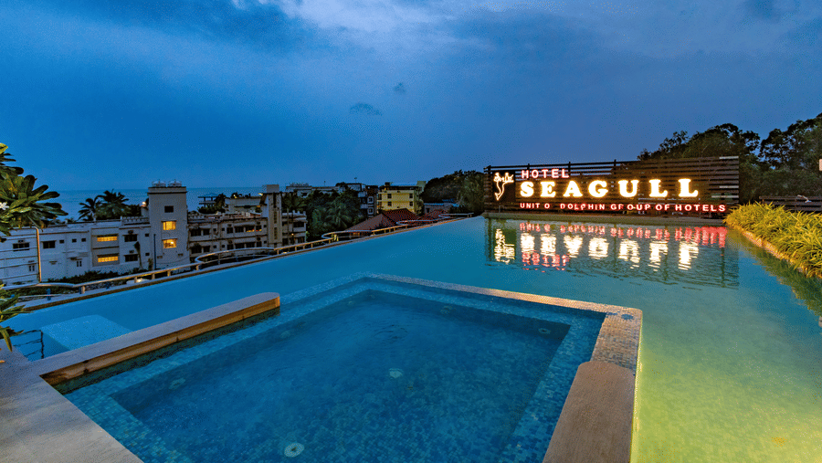 A poolside view with the ‘Seagull’ signage reflected in the swimming pool under a cloudy sky at Hotel Seagull Digha.