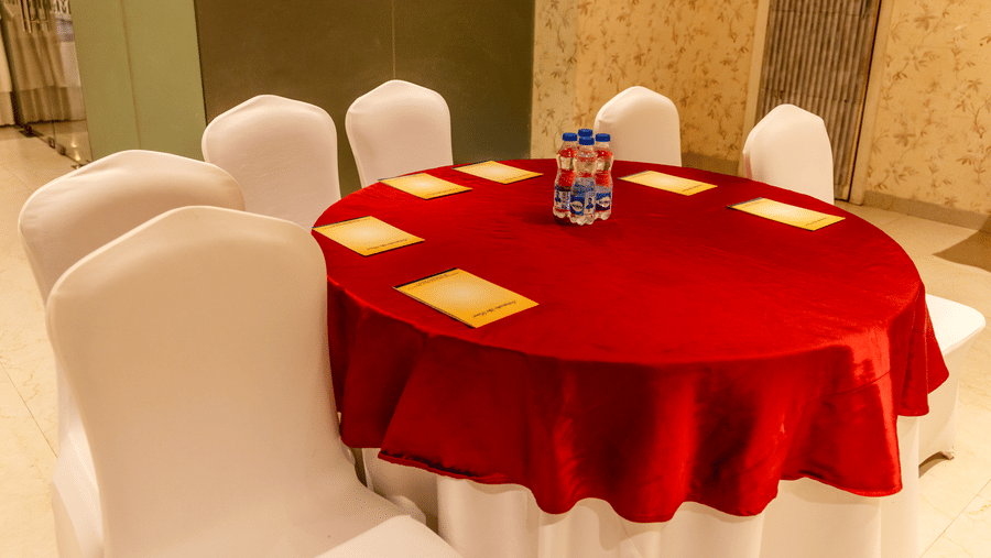 A round table with red tablecloth, chairs, and items placed on top in an indoor setting at Indraprastha Resort & Spa, McLeod Ganj.