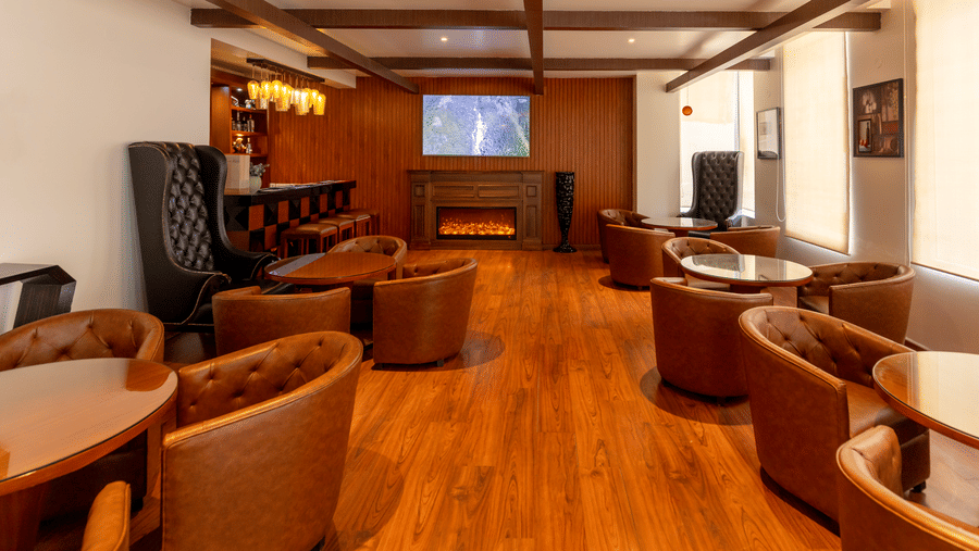 A lounge area with multiple chairs, tables, and a bar counter visible in the background at Indraprastha Resort & Spa, McLeod Ganj.
