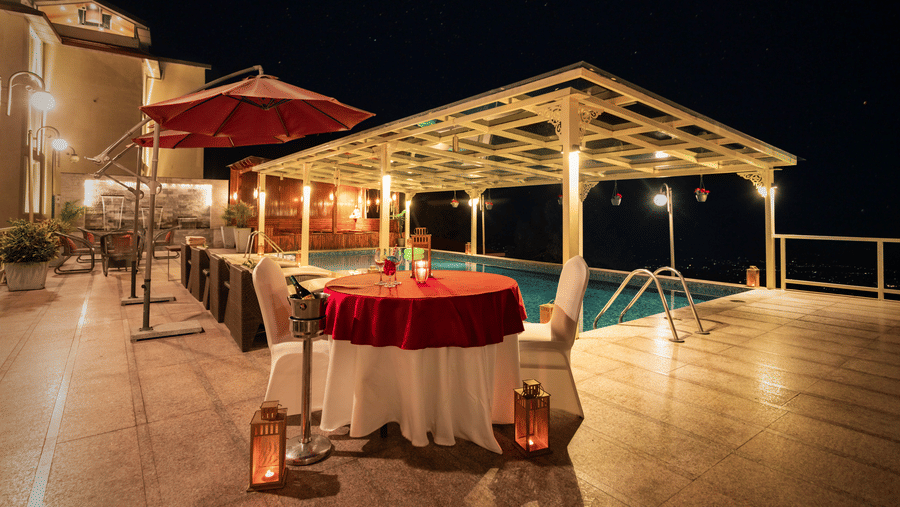 An outdoor dining setup with tables, chairs, lights, and a pool visible nearby at Indraprastha Resort & Spa, McLeod Ganj.