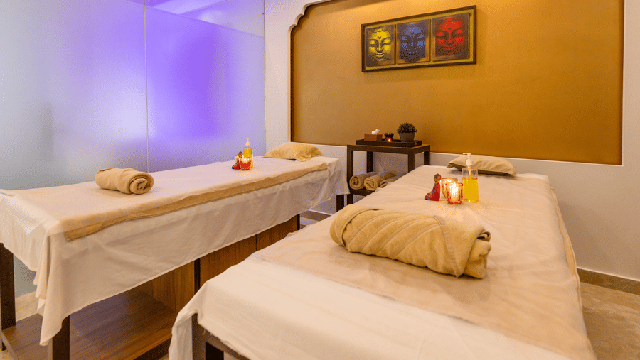 A spa room with 2 massage tables, towels, and wall art arranged indoors at Indraprastha Resort & Spa, McLeod Ganj.