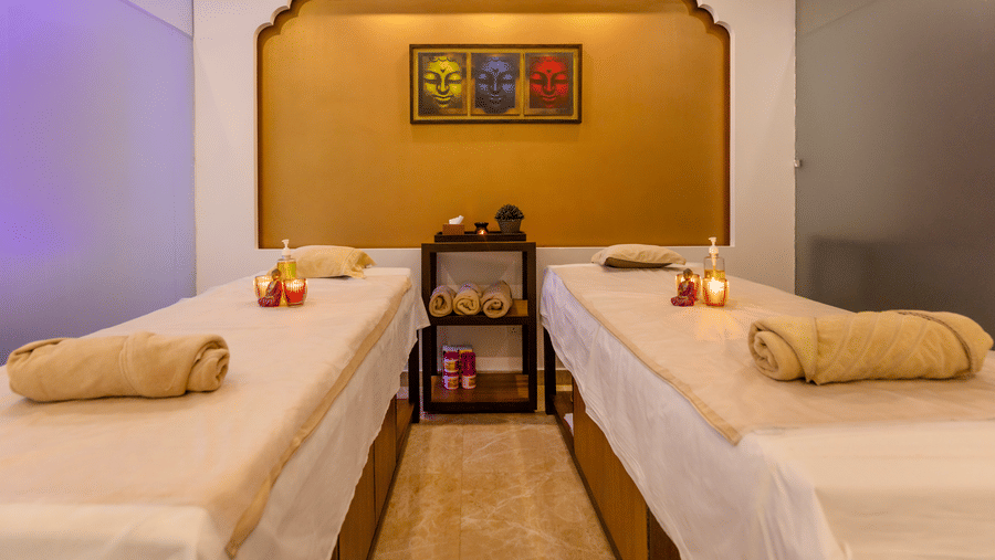 A spa room with 2 massage tables, towels, and decor items arranged indoors at Indraprastha Resort & Spa, McLeod Ganj.