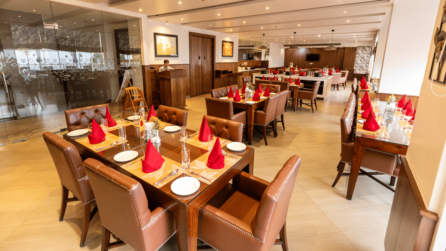 A dining area with multiple tables set with plates, napkins, chairs, and wall decor inside at Indraprastha Resort & Spa, McLeod Ganj.