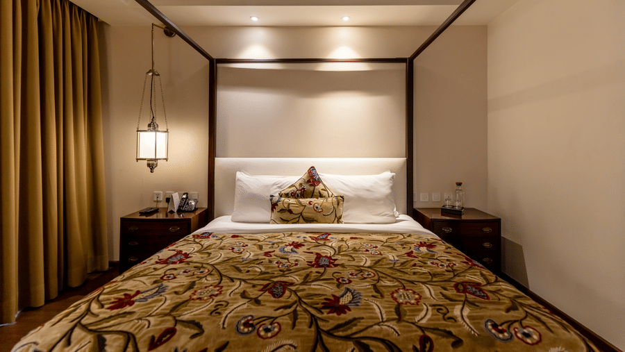 A bedroom with a king size bed, side tables, lamps, and curtains arranged indoors at Indraprastha Resort & Spa, McLeod Ganj.