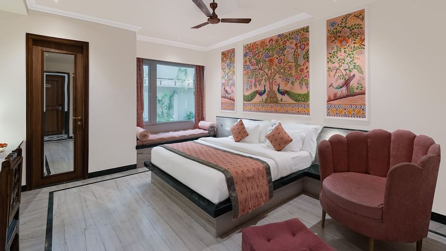 A spacious bedroom at Panna Vilas Palace, featuring a wooden table, cushioned furniture, warm lighting, and a large window