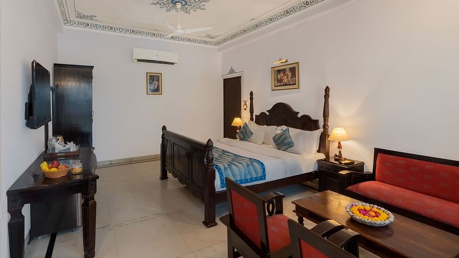 A spacious bedroom featuring a wooden table, cushioned furniture, and warm lighting | Panna Vilas Udaipur
