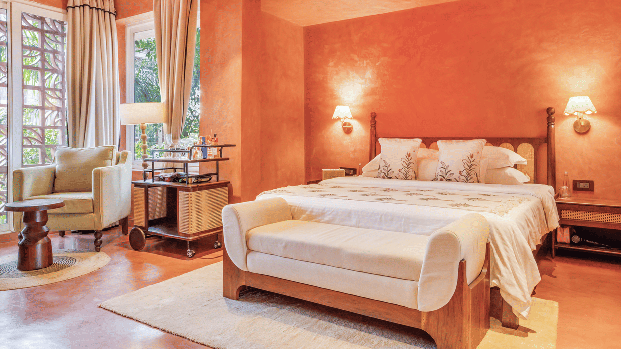 Vibrant bedroom at Unseen Boutique Hotel with bold orange walls, large bed, and natural light creating a lively yet welcoming ambience.