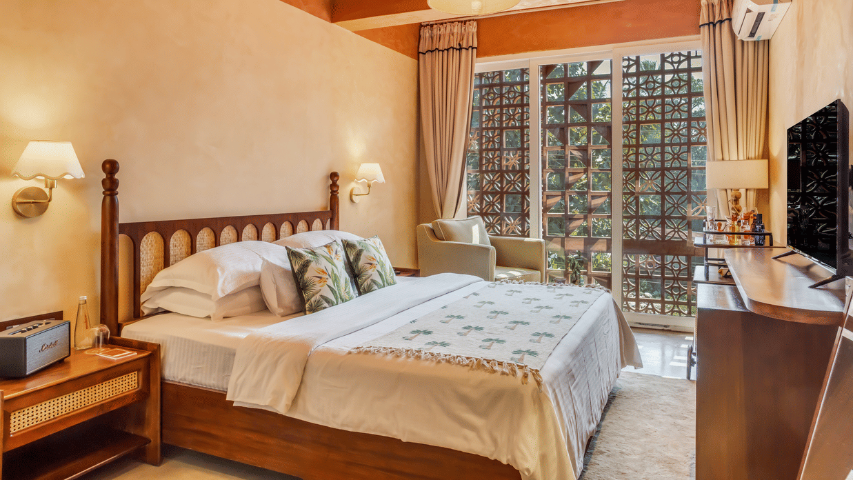 Bedroom at Unseen Boutique Hotel with wooden bed, white and green bedding, bedside lamps, window with curtains, and ceiling light fixture.