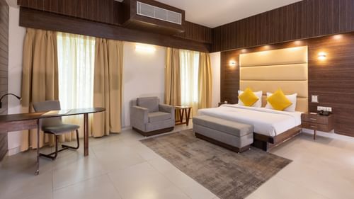 A spacious and elegant hotel bedroom featuring a king-sized bed, a sofa, and stylish lighting - Pride Premier Dehradun