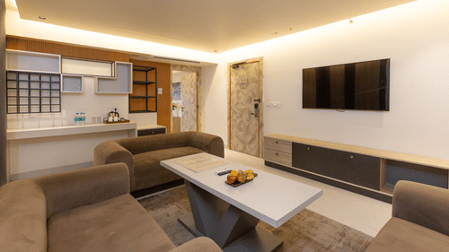 A contemporary hotel suite's living area with comfortable seating, a dining table, and a large television - Pride Premier Dehradun