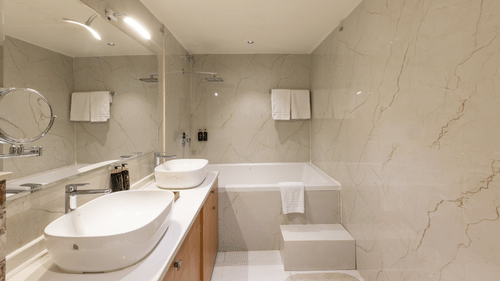 A modern, minimalist hotel bathroom with twin sinks, a large mirror, and a bathtub - Pride Premier Dehradun