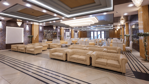 A grand hotel lobby or banquet hall featuring comfortable white sofas and a high, decorative ceiling - Pride Premier Dehradun
