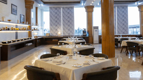 A refined hotel dining room set up for a formal meal, with a buffet table visible on the left - Pride Premier Dehradun