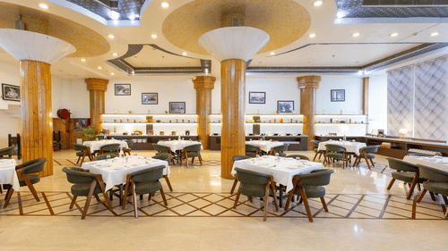 A large, well-lit hotel restaurant with multiple dining tables and a decorative ceiling - Pride Premier Dehradun