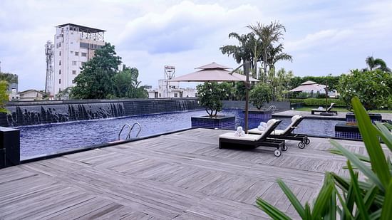 A stylish poolside with lounge chairs, umbrellas, and a serene water feature - Balaji Sarovar Premiere, Solapur