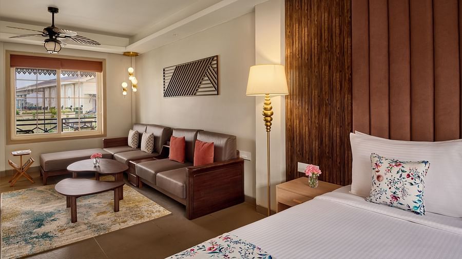 A hotel room featuring a king size bed with a wood-panelled headboard, a patterned rug, and a seating area with a sofa and coffee table. A large window provides natural light - Voyage The Solitaire Bliss.