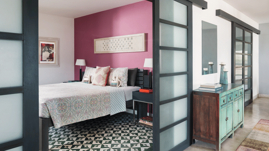 A bedroom at Owl and the Pussycat Hotel in Galle with a bed, patterned flooring, sliding glass doors, and an adjoining sitting area.