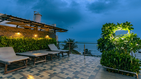 An outdoor seating area with tables, sun loungers, plants and a cloudy sky at Hotel Seagull Digha.