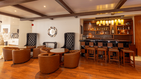A seating area with chairs, tables, and a bar counter visible inside the room at Indraprastha Resort & Spa, McLeod Ganj.
