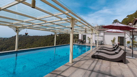 A swimming pool with lounge chairs and a covered structure overlooking hills at Indraprastha Resort & Spa, McLeod Ganj.