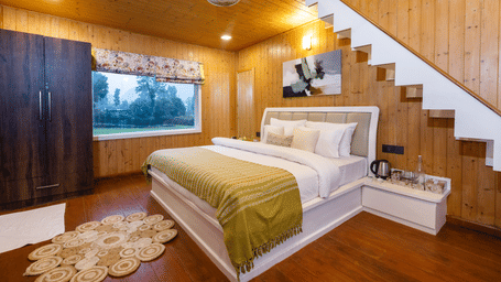 A loft-style bedroom with a bed tucked beneath an open-tread staircase and warm wooden interiors - Megha Resort & Villas, Dehradun
