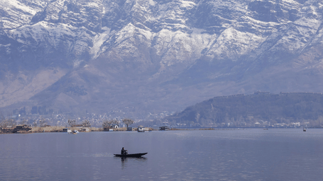 A serene lake with a small boat floating and snow-covered mountains in the background.