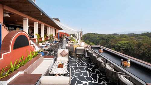 A rooftop terrace with chic outdoor furniture, a striking black and white floor, and lush greenery in the background.