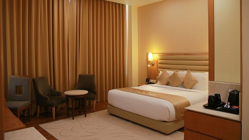 Image of room under warm lighting featuring a plush bed and couches with coffee table next to the window