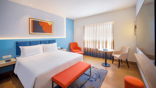 A clean and modern hotel room with a large bed, a desk and chair, and a pop of orange color in the decor | Executive Room | Sarovar Portico, Sriperumbudur