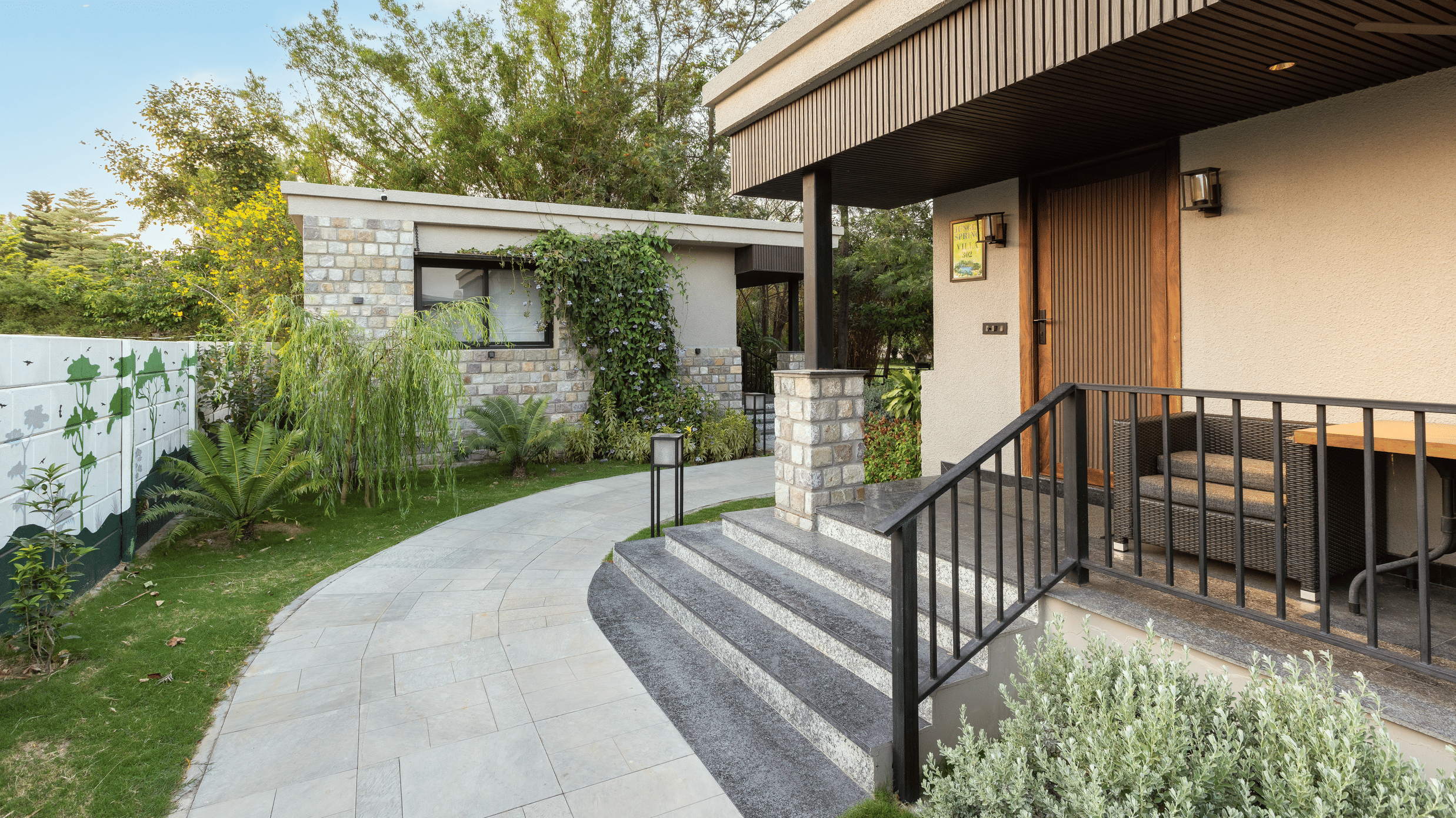 Exterior of jungle spring villa with curved stone pathway leading up to the entrance of a building with stairs and metal railing  at The Golden Tusk, Jim Corbett