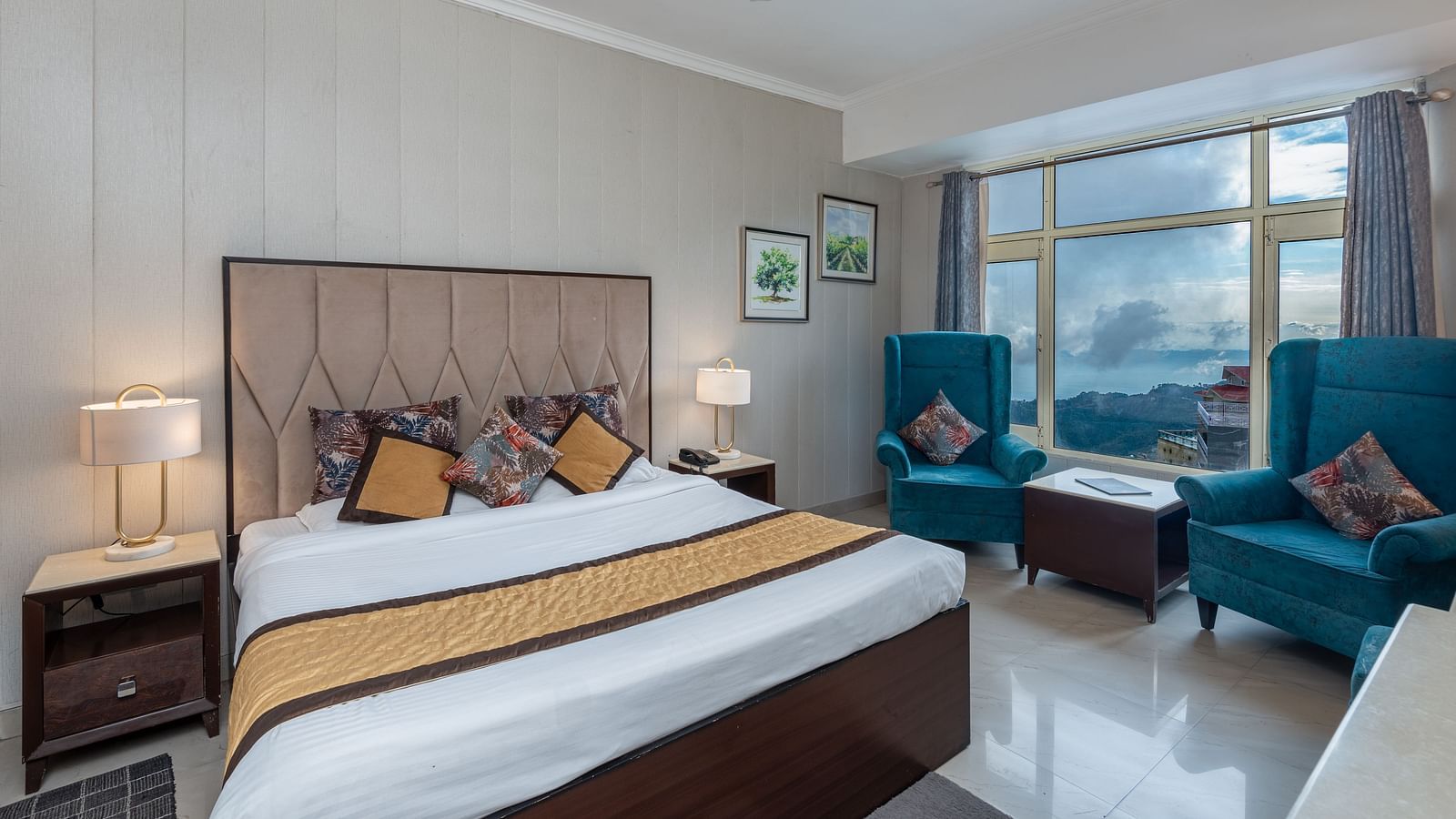 The image shows a hotel room with a large bed, two blue armchairs, a coffee table, and a window with a view | DLS The Pearl