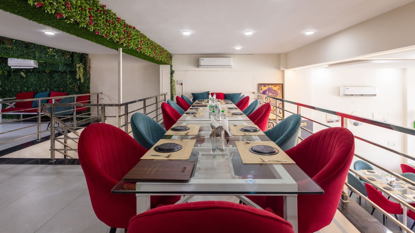 Long dining table setup with red & blue chairs and green decor on the wall at Pravasa Stay Dewas Naka, Indore.