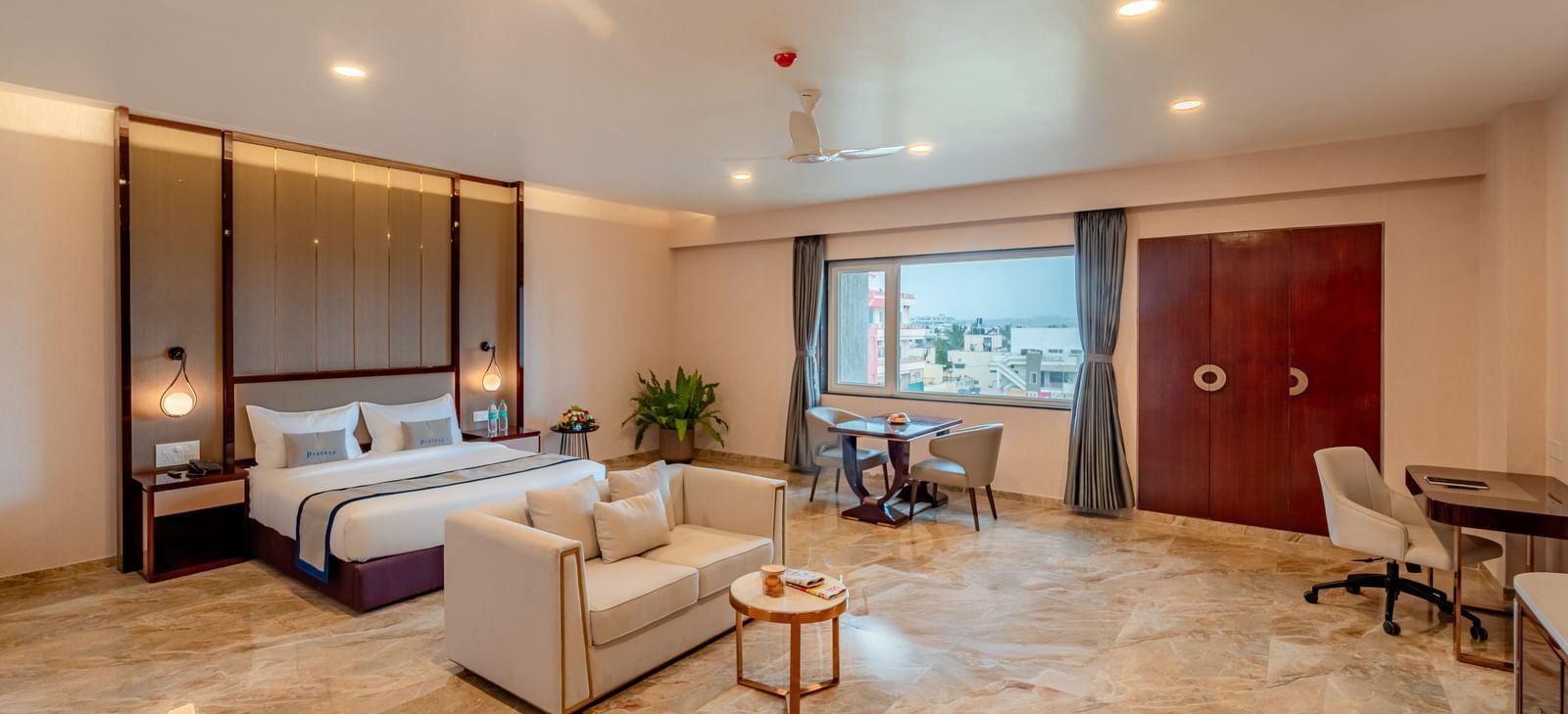 Spacious suite featuring a comfortable bed, a work desk, and city views | Suite | Pravasa Hotel, Vijayapura