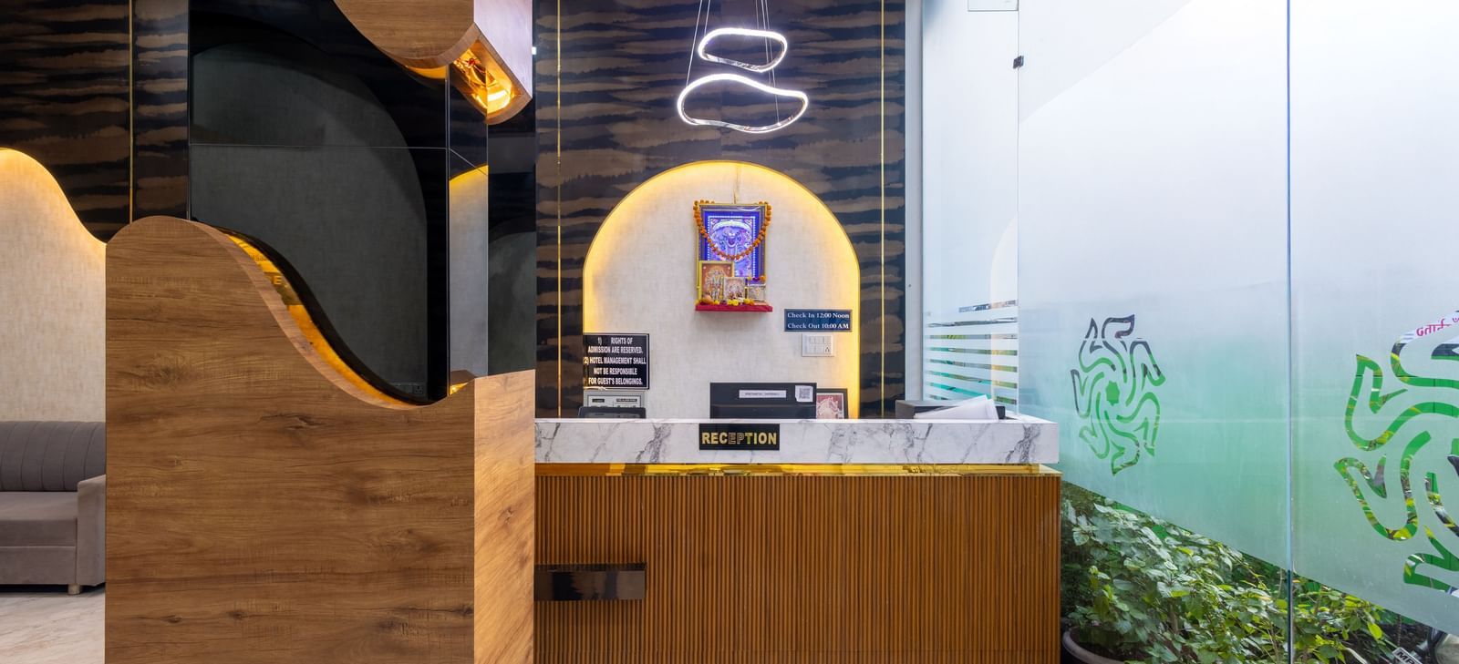 Reception desk with wall art, hanging lights and glass entrance at Pravasa Stay Dewas Naka, Indore.