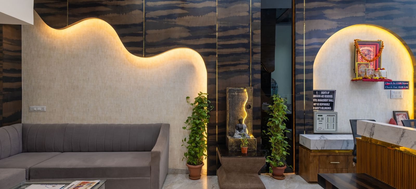 Lobby area with grey sofas, reception desk, and indoor plants at Pravasa Stay Dewas Naka, Indore.