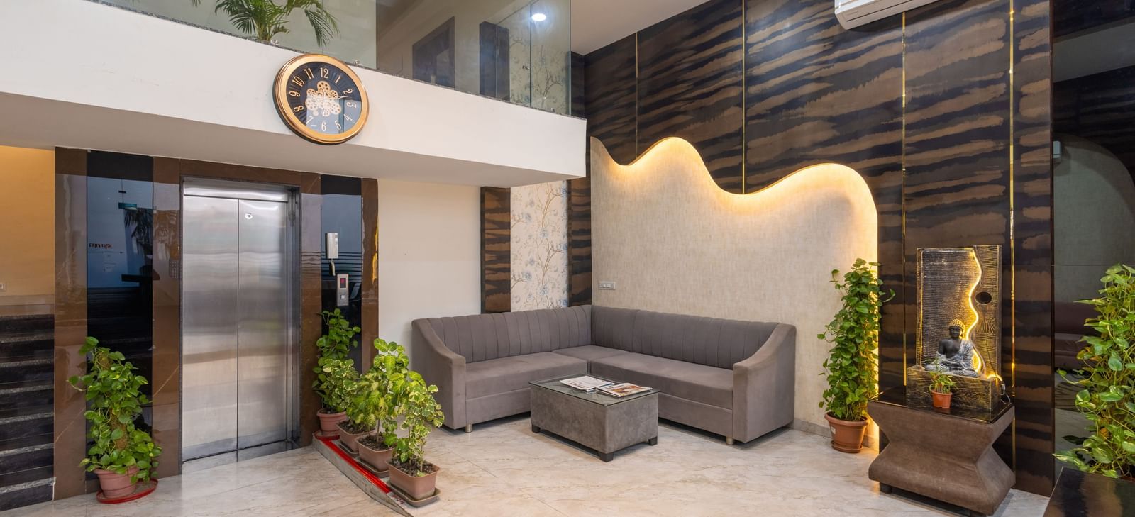 Seating area in a lobby with grey sofas, plants and stylish carved wall at Pravasa Stay Dewas Naka, Indore.