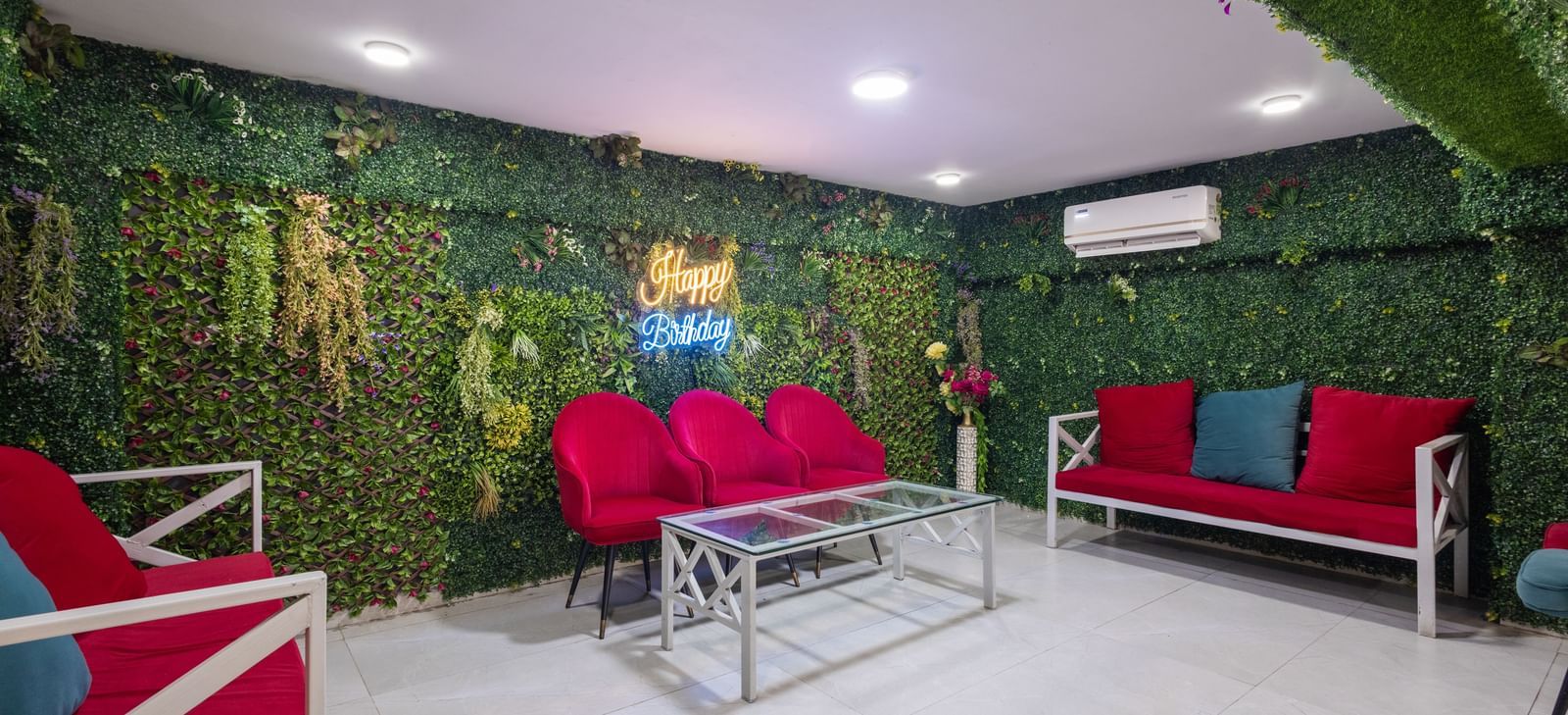 Lounge with red sofas, a glass table, and greenery-covered wall at Pravasa Stay Dewas Naka, Indore.