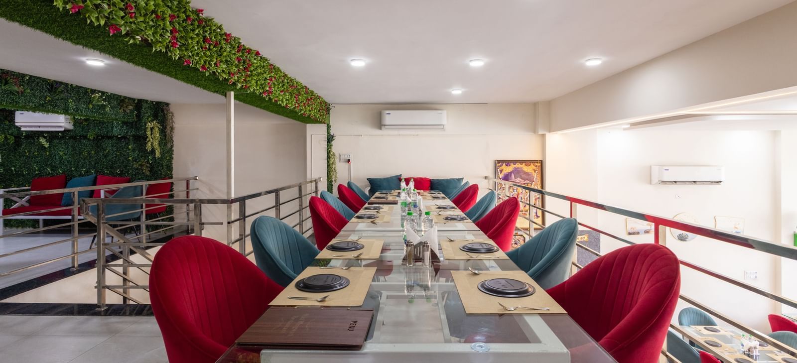 Long dining table setup with red & blue chairs and green decor on the wall at Pravasa Stay Dewas Naka, Indore.