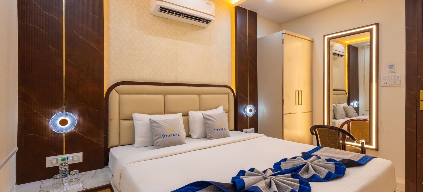 A well lit room with a double bed, side tables, mirror with a chair, and air conditioning at Pravasa Stay Dewas Naka, Indore.