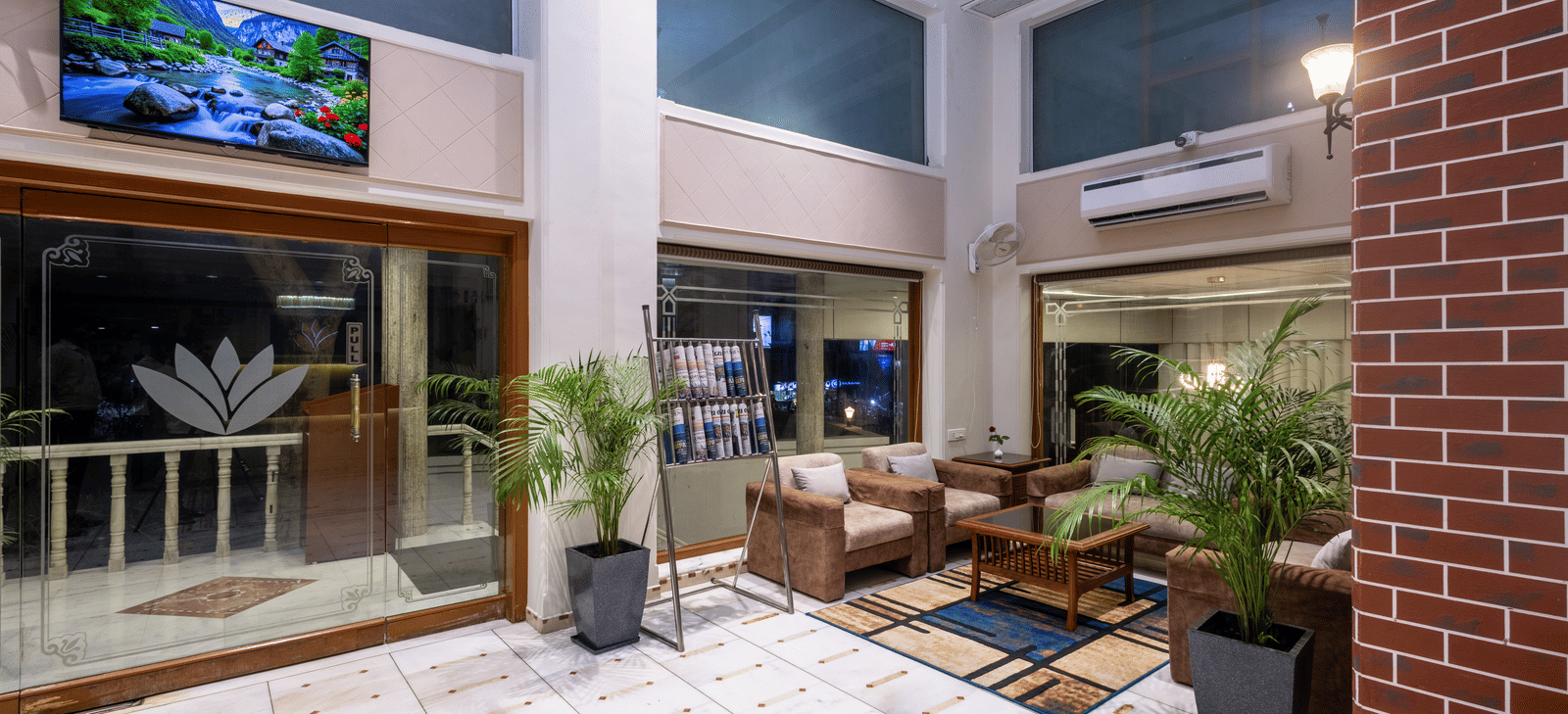 View of a patio/courtyard area with seating and plants, looking towards the hotel interior through glass doors at Pravasa Stay, Vadodara.